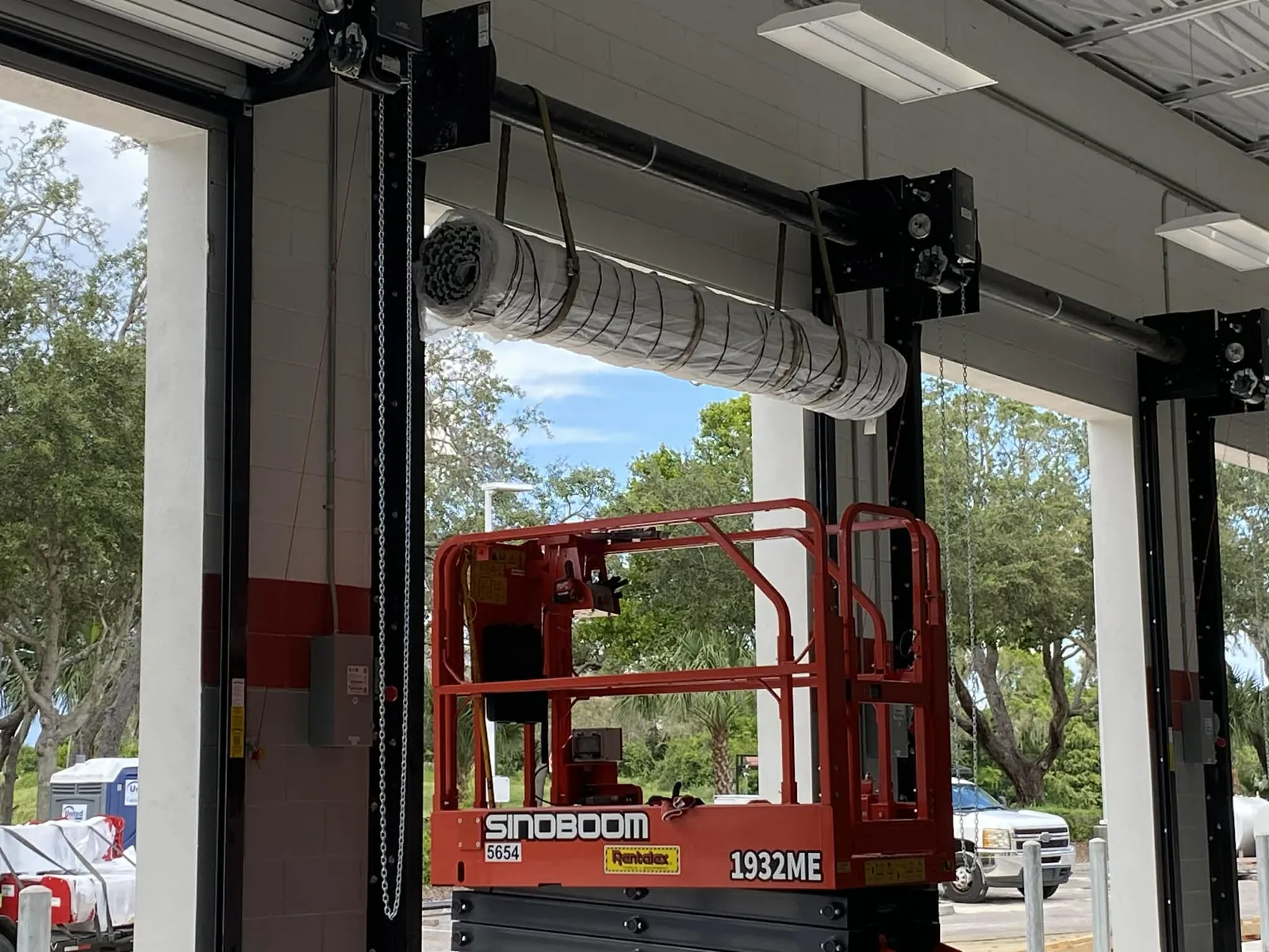 Jackshaft operators and chain hoists mounted above tall apparatus bay openings, live oaks and sabal palms visible through the doorways