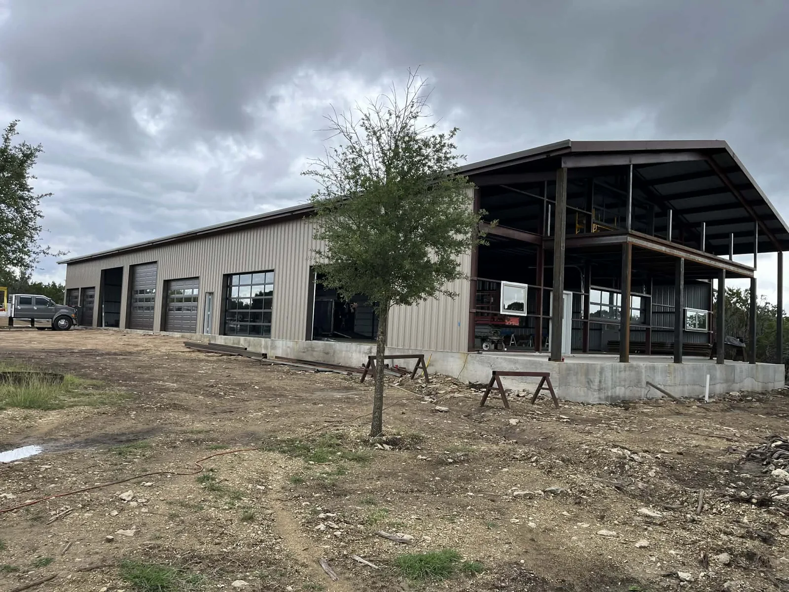 Contractor shop with sectional doors at one end and full-view glass openings at the other, an open-air steel canopy framed onto the same slab