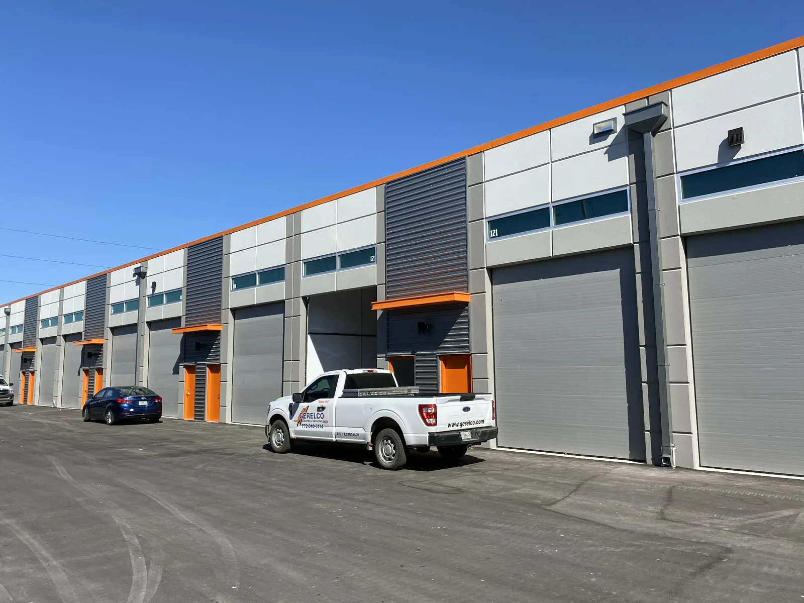 Row of insulated steel sectional bay doors along a new flex industrial park, one unit open and the rest closed to the drive aisle