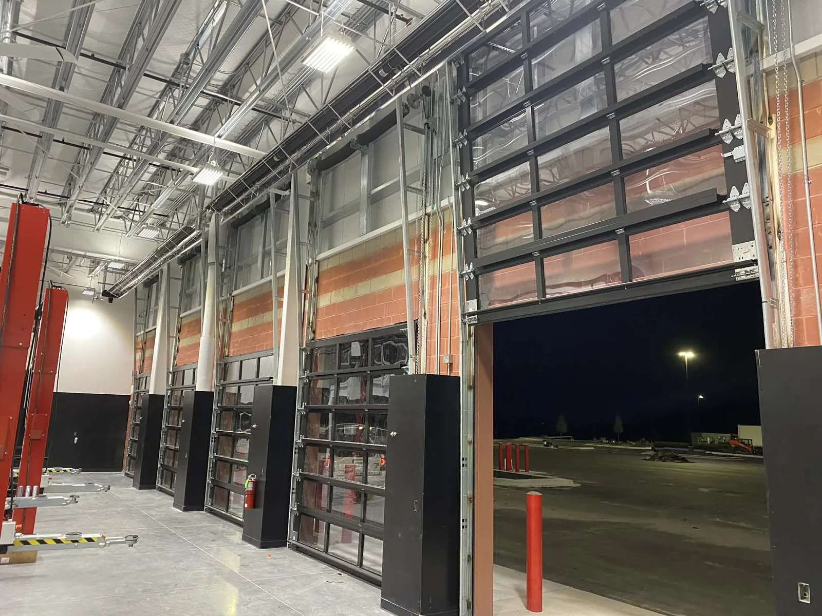 Full-view glass sectional doors seen from inside a service bay during installation, protective film still on the panels and chain hoists hung at each jamb