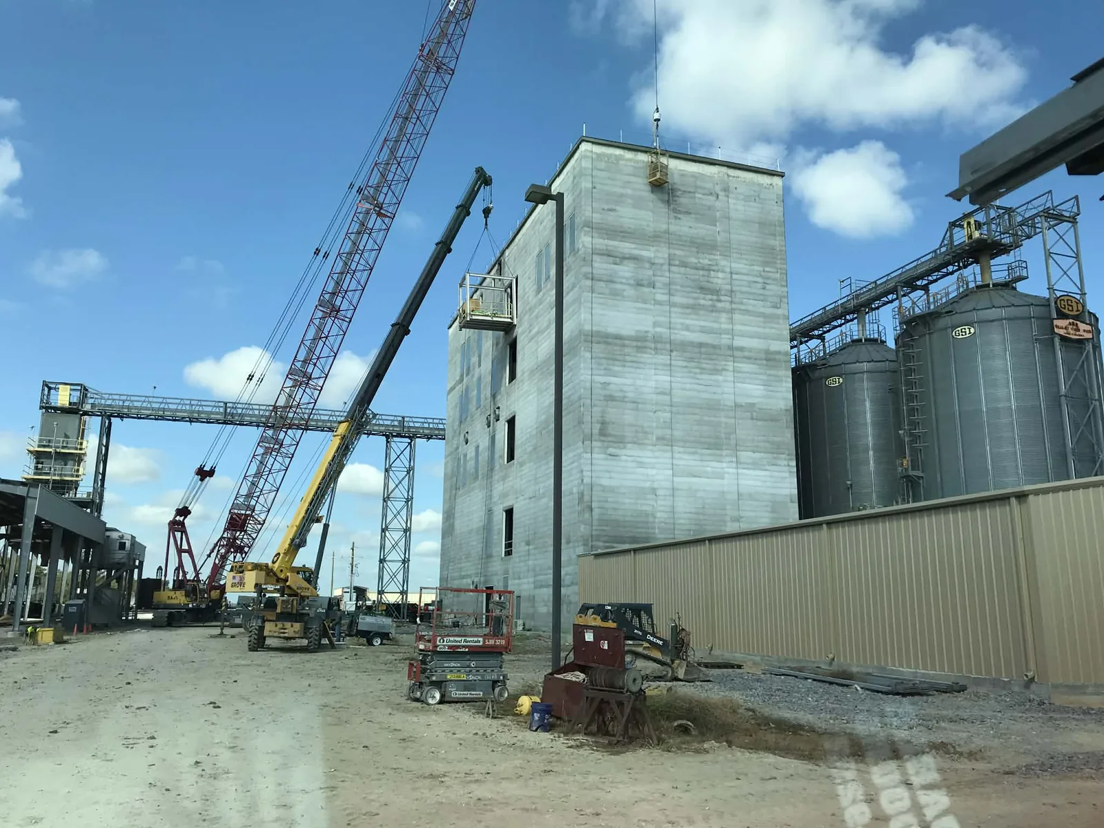 Grain handling facility mid-build with the concrete tower topped out, cranes on the pad and a conveyor gallery running to the storage bins